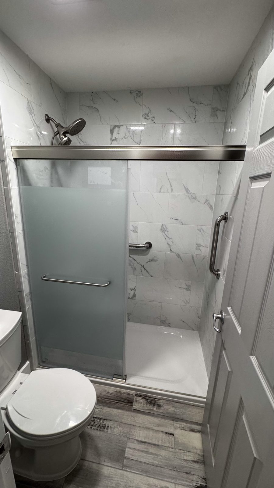 Glass walk-in shower with marble tile and wood-look flooring